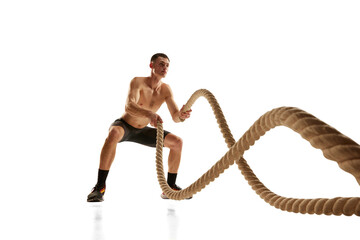 Portrait of strong young man practicing with battle ropes during workout isolated over white background. Fitness, healthy and active lifestyle concept