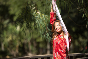 Obraz premium Beautiful young woman in a typical Moroccan red suit, embroidered with gold and silver threads, holding a scarf with coins in her hands, on a wooden bridge. Concept beauty, ethnicity, Marrakech, Arab