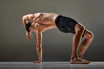 Portrait of male flexible muscular athlete showing animal flow sport elements isolated over gray...