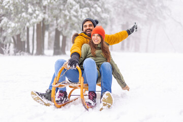 Couple sitting on sled and sliding down the hill while on winter vacation - obrazy, fototapety, plakaty