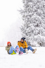 Fototapeta na wymiar Couple sliding down the hill in the snow while on winter vacation