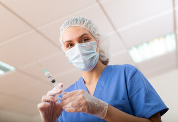 Female nurse or doctor wearing in face mask and medical uniform holding vial and syringe