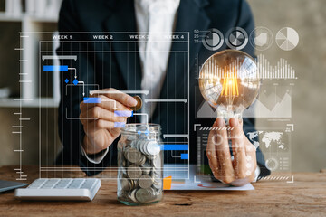 business hand holding lightbulb with using laptop computer and money stack in office. idea saving...