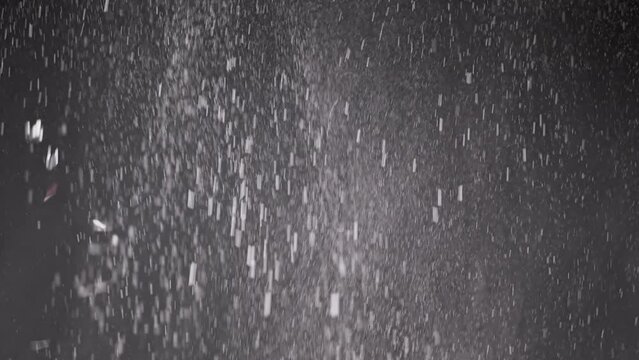 Stream of Falling Confetti, Dust Particles, and Snowfall on Black Background. Blurred abstract dynamic background of flying tinsel, snowflakes, white powder in cloudy mist smoke. Stardust, fireworks.