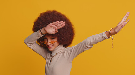 Fototapeta na wymiar Trendy cheerful positive young school girl with afro hairstyle having fun dancing and moving to rhythm, dabbing raising hands, making dubdance gesture. Teenager female child kid on yellow background