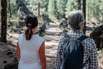Obraz premium Back view of two mature women enjoying hike in the woods walking in footpath. Elderly retired females and adventure ageless concept