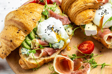 Spanish breakfast, Croissant Toast or sandwich with Poached egg, jamon, blue, cheese, avocado, microgin and cherry tomatoes, Cup of coffee, Food recipe background. vertical image