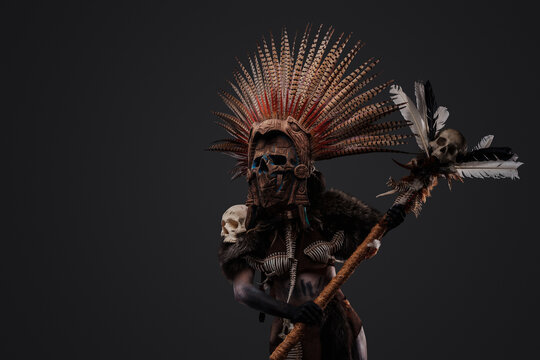 Shot of scary aztec necromancer holding staff with skull against grey background.