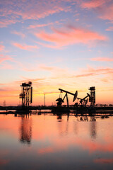 Fototapeta na wymiar in the evening, oil pumps are running, The oil pump and the beautiful sunset reflected in the water, the silhouette of the beam pumping unit in the evening.