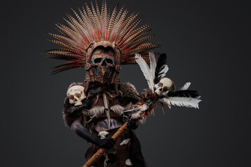 Fototapeta premium Photo of aztec witch from past with plumed headdress and mask holding staff with skull head.