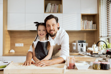 Delighted family father and daughter looking at camera smiling wearing aprons kneading homemade dough for baking cooking pizza preparing surprise dinner for family.