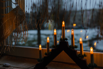 Glowing menorah on the windowsill.Winter background of dark windows and curtains.Electric candles,decoration on the windowsill,preparations for Christmas,reflection of candlelight in the windowsglass.
