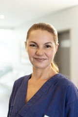 Vertical portrait of smiling caucasian female healthcare worker in corridor, with copy space