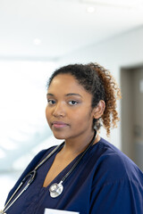 Fototapeta premium Vertical portrait of african american female doctor in hospital corridor, with copy space