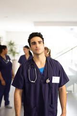 Vertical of serious biracial male doctor walking in busy hospital corridor, with copy space