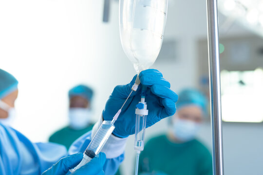 Gloved hand of surgical tech preparing iv fluid bag in operating theatre, with copy space