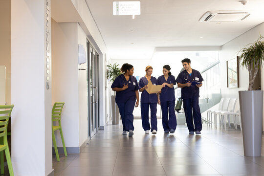 Diverse Group Of Happy Male And Female Doctors Talking Walking In Hospital Corridor, With Copy Space