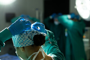 Rear view of biracial female surgeon in gloves and cap tying mask in theatre, with copy space - Powered by Adobe