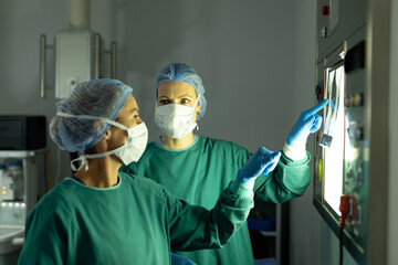 Fototapeta na wymiar Two diverse female surgeons preparing for operation, discussing x-ray in operating theatre
