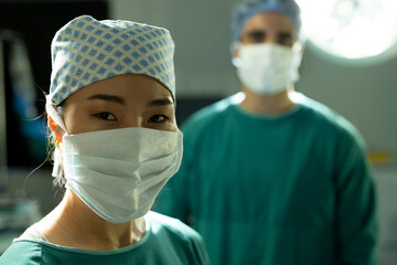 Portrait of happy asian female surgeon in surgical cap and mask in operating theatre with colleague