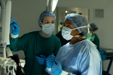Diverse female surgeons in discussion, using medical equipment in operating theatre during operation