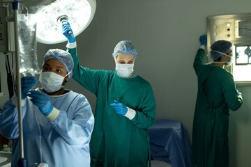 Fototapeta na wymiar Two diverse female surgical techs adjusting light and iv bag in operating theatre during operation