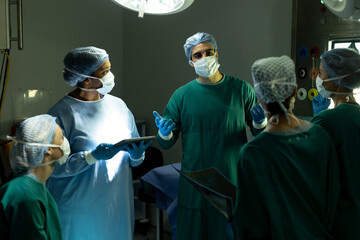 Diverse group of surgeons in discussion, using tablet in operating theatre before operation