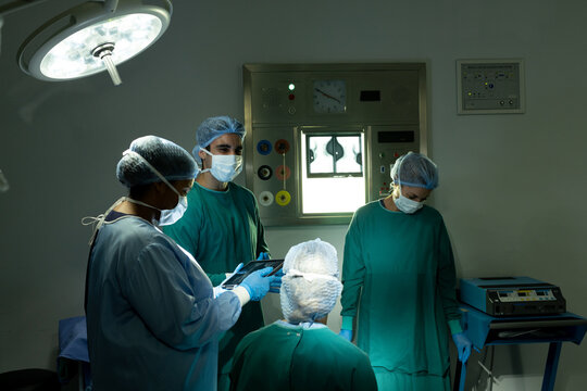 Diverse group of surgeons in discussion, using tablet in operating theatre before operation
