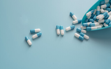 Blue-white capsule pills spread out of plastic spoon on blue background. Prescription drug....