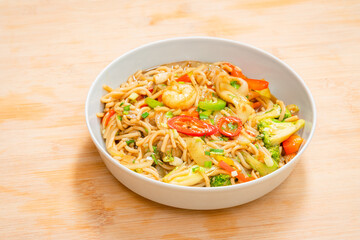 Golden coloured spicy sea food noodles with shrimp, broccoli, chilli pepper in a plate on wooden table