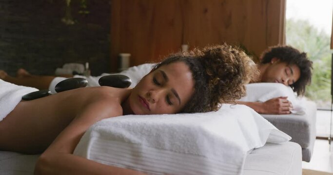 Video of relaxed diverse couple having hot stone massage treatment at health spa