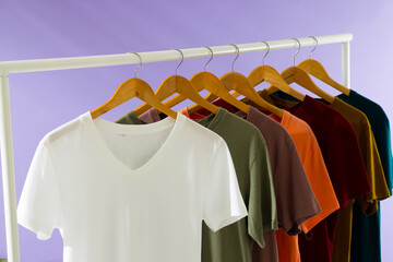Fototapeta premium Coloured tshirts displayed on clothing rail and copy space on purple background