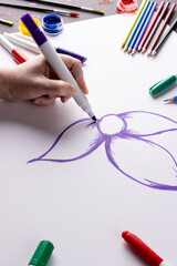 Vertical image of hand drawing purple flower on paper and art materials on table top, copy space