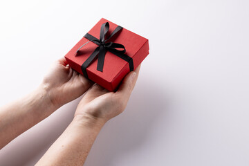 Hands holding red gift box tied with black ribbon, on white background with copy space