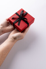 Vertical of hands holding red gift box tied with black ribbon, on white background with copy space