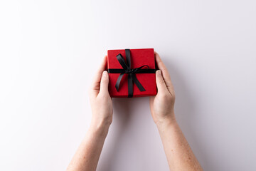 Hands presenting red gift box tied with black ribbon, on white background with copy space