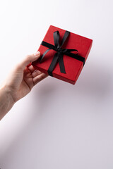Vertical of hand giving red gift box tied with black ribbon, on white background with copy space