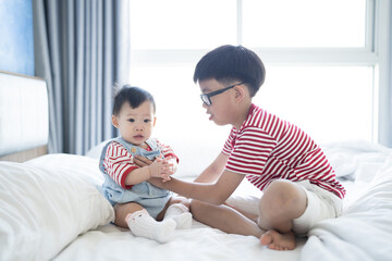 Brother and baby sister is playing on the white bed in the bedroom.The selective focus and space...