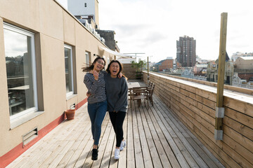 Young laughing women hugging and walking and bouncing on wooden terrace with view of Barcelona.
