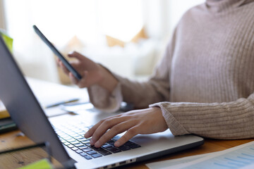 Midsection of biracial woman wearing hijab, sitting at table, using laptop and smartphone