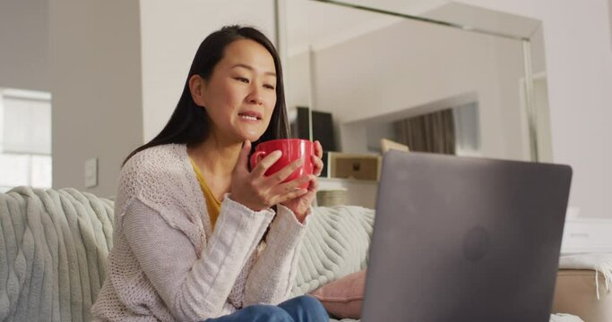Video of happy asian woman wit coffee using laptop
