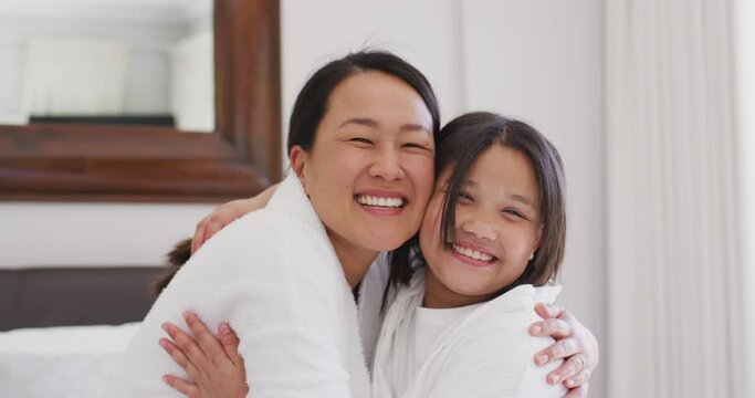 Video of happy asian mother and daughter in robes embracing and having fun