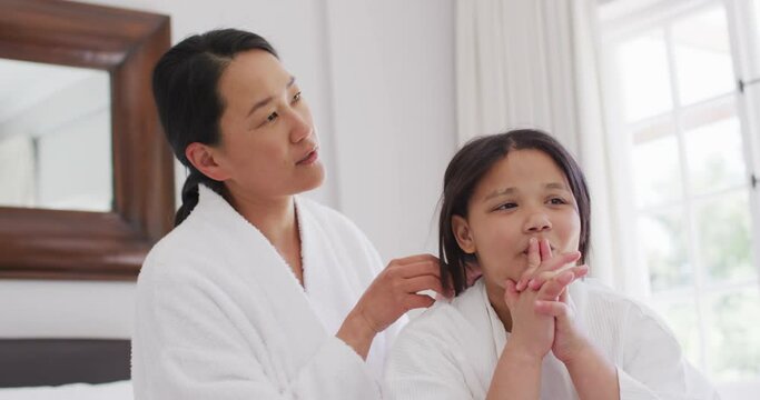 Video of happy asian mother and daughter in robes having fun