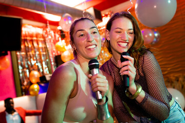 Two happy caucasian female friends singing karaoke at a nightclub bar
