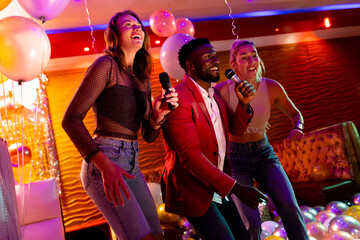 Three diverse male and female friends having fun singing karaoke at a nightclub bar