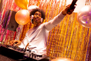 Smiling african american dj in headphones playing music at a nightclub and holding microphone