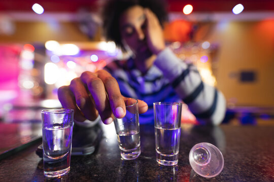 Drunk african american man sitting at the bar with shot glasses, selective focus