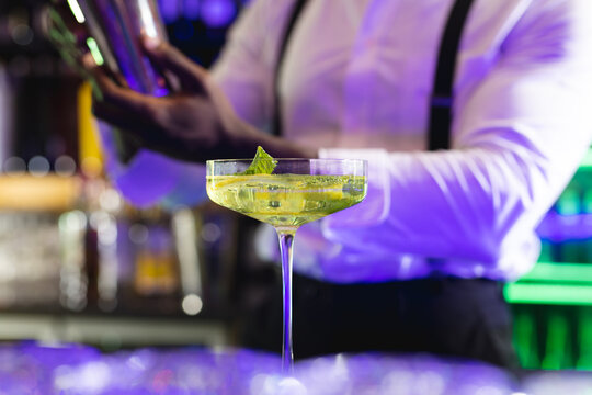 Midsection of african american barman preparing green cocktail at a bar, selective focus