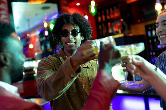 Happy group of diverse male and female friends drinking by the bar at a nightclub making a toast