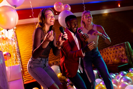 Three diverse male and female friends having fun singing karaoke at a nightclub bar